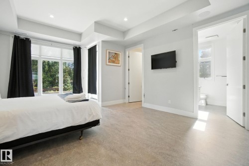 Bedroom with a tray ceiling, concrete flooring, connected bathroom, and recessed lighting - 11823 Saskatchewan Drive, Edmonton, AB - Indoor Photo Showing Bedroom