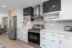 Kitchen with glass insert cabinets, appliances with stainless steel finishes, wall chimney range hood, tasteful backsplash, and recessed lighting - 