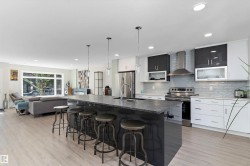 Kitchen featuring a breakfast bar, an island with sink, stainless steel appliances, open floor plan, and wall chimney range hood - 