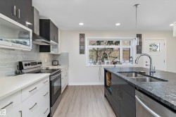 Kitchen with appliances with stainless steel finishes, pendant lighting, dark stone counters, wall chimney exhaust hood, and light wood-style floors - 