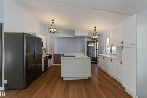 Kitchen featuring white cabinets, appliances with stainless steel finishes, light countertops, pendant lighting, and dark wood-style flooring - 6808 95 Avenue, Edmonton, AB - Indoor Photo Showing Kitchen