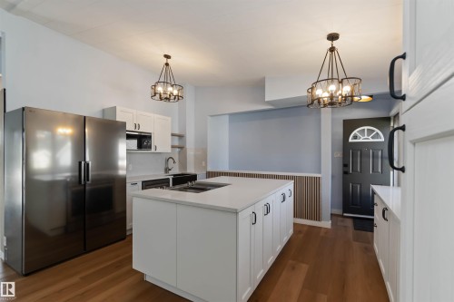 Kitchen with white cabinetry, stainless steel appliances, dark wood-style flooring, wainscoting, and a chandelier - 6808 95 Avenue, Edmonton, AB - Indoor Photo Showing Kitchen
