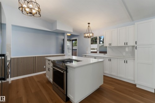 Kitchen with a chandelier, stainless steel appliances, white cabinetry, hanging light fixtures, and wainscoting - 6808 95 Avenue, Edmonton, AB - Indoor Photo Showing Kitchen