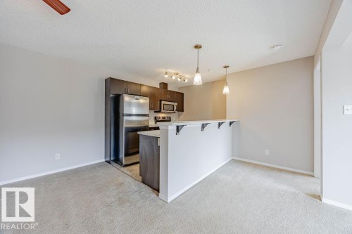 Kitchen with appliances with stainless steel finishes, dark brown cabinets, hanging light fixtures, a kitchen breakfast bar, and light carpet - Edmonton, AB - Indoor Photo Showing Kitchen