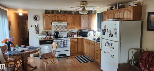 Kitchen featuring white appliances, light countertops, brown cabinets, light wood-style floors, and tasteful backsplash - 5002 - 50 Avenue, Dapp, AB - Indoor Photo Showing Kitchen With Double Sink