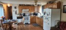 Kitchen featuring white appliances, light countertops, brown cabinets, light wood-style floors, and tasteful backsplash - 5002 - 50 Avenue, Dapp, AB  - Indoor Photo Showing Kitchen With Double Sink 