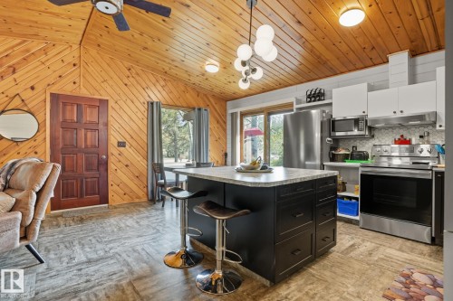 Kitchen with a kitchen breakfast bar, appliances with stainless steel finishes, dark cabinetry, pendant lighting, and wood walls - 6309 49 St, Rural Wetaskiwin County, AB - Indoor Photo Showing Kitchen