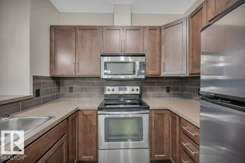 Kitchen with appliances with stainless steel finishes, brown cabinetry, backsplash, and light countertops - 140 308 Ambleside Link, Edmonton, AB - Indoor Photo Showing Kitchen