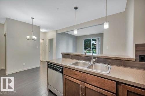 Kitchen featuring decorative light fixtures, dishwasher, dark wood-style floors, a chandelier, and light countertops - 140 308 Ambleside Link, Edmonton, AB - Indoor Photo Showing Kitchen With Double Sink