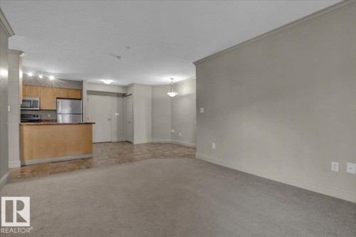 Unfurnished living room with light colored carpet, a textured ceiling, ornamental molding, and light tile patterned floors - 226 13111 140 Avenue, Edmonton, AB - Indoor