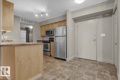 Kitchen with stainless steel appliances, a textured ceiling, a peninsula, stone finish flooring, and light brown cabinetry - 226 13111 140 Avenue, Edmonton, AB - Indoor Photo Showing Kitchen