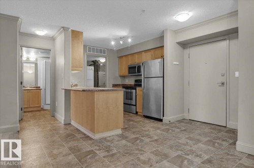 Kitchen featuring appliances with stainless steel finishes, a peninsula, a textured ceiling, ornamental molding, and light brown cabinetry - 226 13111 140 Avenue, Edmonton, AB - Indoor Photo Showing Kitchen
