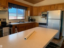 Kitchen with stainless steel appliances, brown cabinets, light countertops, under cabinet range hood, and lofted ceiling - 