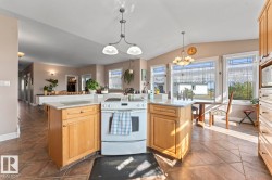 Kitchen featuring white range with electric stovetop, vaulted ceiling, hanging light fixtures, light stone counters, and stainless steel microwave - 