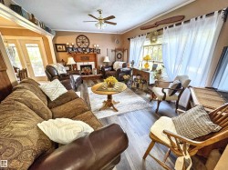 Living area featuring a textured ceiling, wood finished floors, a fireplace with raised hearth, ceiling fan, and crown molding - 