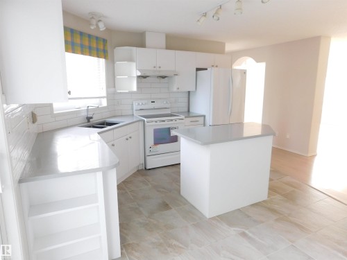 Kitchen with open shelves, tasteful backsplash, white appliances, a center island, and white cabinets - 26 1295 Carter Crest Road, Edmonton, AB - Indoor Photo Showing Kitchen With Double Sink