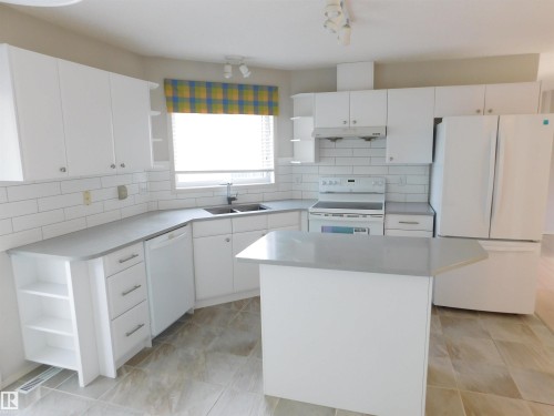Kitchen featuring open shelves, white appliances, a kitchen island, and decorative backsplash - 26 1295 Carter Crest Road, Edmonton, AB - Indoor Photo Showing Kitchen With Double Sink