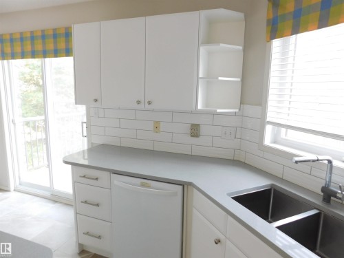 Kitchen with open shelves, dishwasher, white cabinetry, tasteful backsplash, and light stone counters - 26 1295 Carter Crest Road, Edmonton, AB - Indoor Photo Showing Kitchen With Double Sink
