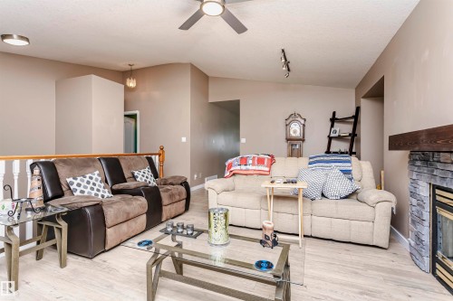 Living area with vaulted ceiling, light wood-style floors, a stone fireplace, a textured ceiling, and ceiling fan - 8 Lafond Drive, Tofield, AB - Indoor Photo Showing Living Room With Fireplace