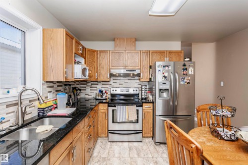 Kitchen with stainless steel appliances, decorative backsplash, dark stone countertops, and under cabinet range hood - 8 Lafond Drive, Tofield, AB - Indoor Photo Showing Kitchen With Double Sink