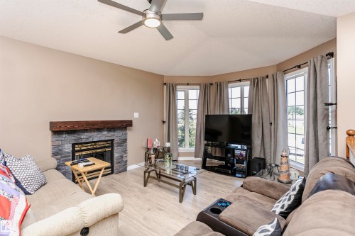 Living room with light wood-type flooring, healthy amount of natural light, a fireplace, a textured ceiling, and a ceiling fan - 8 Lafond Drive, Tofield, AB - Indoor Photo Showing Living Room With Fireplace