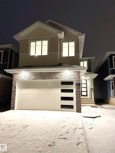 View of front facade with stone siding, a garage, concrete driveway, and board and batten siding - 3154 Magpie Way, Edmonton, AB - Outdoor