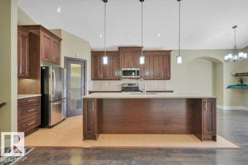 Kitchen featuring stainless steel appliances, decorative backsplash, light wood-style flooring, decorative light fixtures, and a center island with sink - 6221 167A Avenue, Edmonton, AB - Indoor Photo Showing Kitchen With Upgraded Kitchen