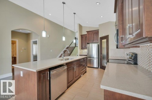 Kitchen featuring an island with sink, appliances with stainless steel finishes, hanging light fixtures, tasteful backsplash, and light stone counters - 6221 167A Avenue, Edmonton, AB - Indoor Photo Showing Kitchen With Double Sink