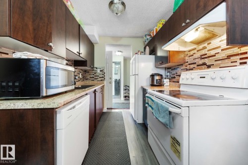 Kitchen featuring white appliances, under cabinet range hood, light countertops, dark brown cabinets, and a textured ceiling - 285 Harrison Drive, Edmonton, AB - Indoor Photo Showing Kitchen