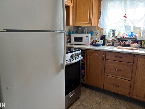 Kitchen with white appliances, tasteful backsplash, brown cabinetry, and light countertops - 140 Russel Drive, Rural St. Paul County, AB - Indoor Photo Showing Kitchen