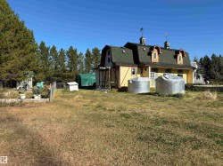 Back of property with a gambrel roof, a yard, and view of wooded area - 