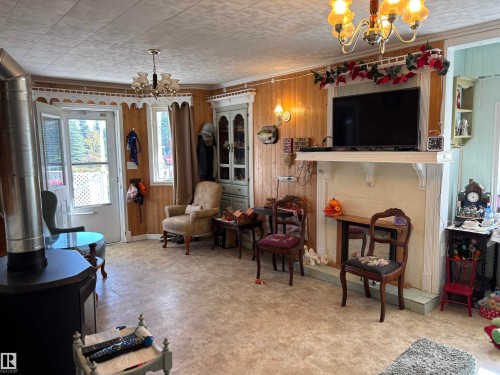 Sitting room with a chandelier, wooden walls, crown molding, a tile fireplace, and a wood stove - 140 Russel Drive, Rural St. Paul County, AB - Indoor