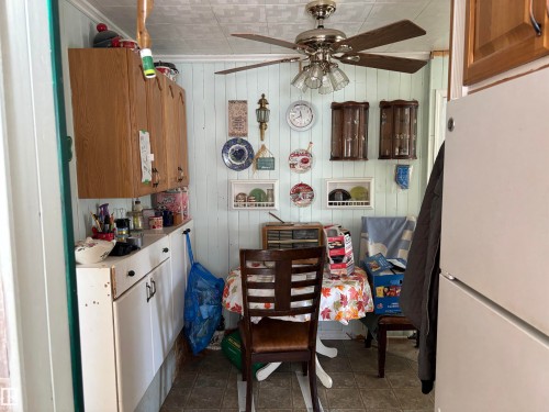 Kitchen featuring freestanding refrigerator, wood walls, light countertops, ceiling fan, and dark tile patterned flooring - 140 Russel Drive, Rural St. Paul County, AB - Indoor