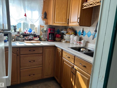 Kitchen with backsplash, brown cabinetry, light countertops, fridge, and dark tile patterned flooring - 140 Russel Drive, Rural St. Paul County, AB - Indoor Photo Showing Kitchen With Double Sink
