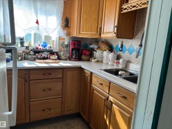 Kitchen with backsplash, brown cabinetry, light countertops, fridge, and dark tile patterned flooring - 