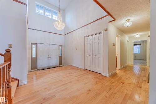 Foyer with light wood-style floors, a chandelier, a textured ceiling, a towering ceiling, and stairway - 1602 106 Street, Edmonton, AB - Indoor Photo Showing Other Room