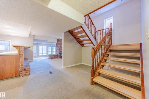 Stairs with carpet flooring, a textured ceiling, and a brick fireplace - 1602 106 Street, Edmonton, AB - Indoor Photo Showing Other Room