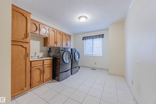 Laundry room featuring a textured ceiling, light tile patterned flooring, washer and dryer, and cabinet space - 1602 106 Street, Edmonton, AB - Indoor Photo Showing Laundry Room