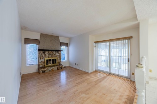 Unfurnished living room with light wood-style flooring, a fireplace, and a textured ceiling - 1602 106 Street, Edmonton, AB - Indoor Photo Showing Other Room With Fireplace
