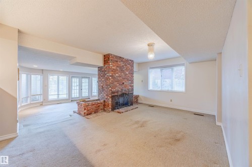 Unfurnished living room featuring carpet floors, a textured ceiling, and a brick fireplace - 1602 106 Street, Edmonton, AB - Indoor With Fireplace