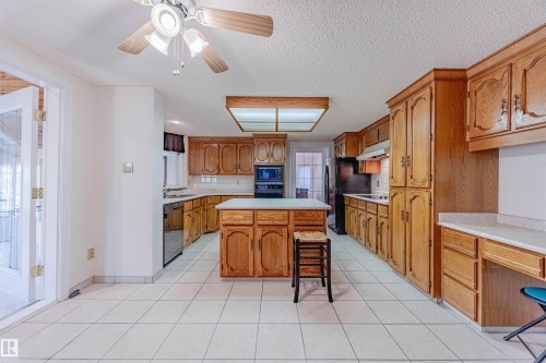 Kitchen featuring brown cabinets, light countertops, a kitchen bar, a textured ceiling, and a kitchen island - 1602 106 Street, Edmonton, AB - Indoor Photo Showing Kitchen