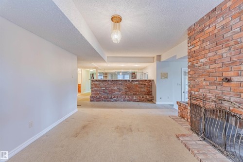 Unfurnished living room featuring carpet floors, a textured ceiling, and a fireplace - 1602 106 Street, Edmonton, AB - Indoor Photo Showing Other Room With Fireplace