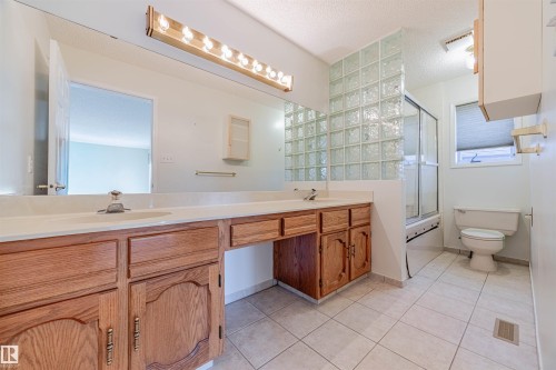 Full bath with light tile patterned flooring, double vanity, bath / shower combo with glass door, and a textured ceiling - 1602 106 Street, Edmonton, AB - Indoor Photo Showing Bathroom