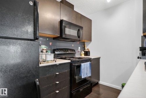 Kitchen with black appliances, backsplash, dark wood-style flooring, a textured ceiling, and light countertops - 209 3353 16A, Edmonton, AB - Indoor Photo Showing Kitchen