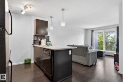 Kitchen with a peninsula, light countertops, dark wood-type flooring, black fridge, and hanging light fixtures - 