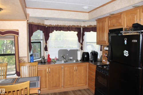 Kitchen with black appliances, ornamental molding, dark countertops, light wood-style floors, and brown cabinetry - #544 12002 Twp Rd 605A, Rural St. Paul County, AB 