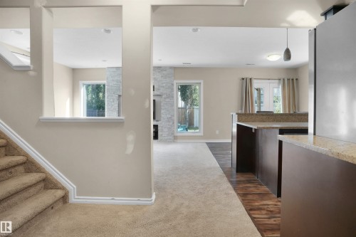Kitchen with hanging light fixtures, dark carpet, light stone counters, a stone fireplace, and dark brown cabinets - 20705 56A Avenue, Edmonton, AB - Indoor Photo Showing Other Room