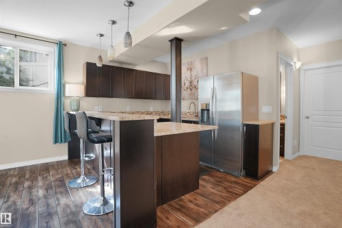 Kitchen featuring a kitchen bar, dark brown cabinetry, stainless steel refrigerator with ice dispenser, pendant lighting, and dark wood-style flooring - 20705 56A Avenue, Edmonton, AB - Indoor Photo Showing Kitchen