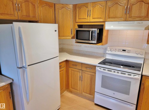Kitchen with white appliances, exhaust hood, light countertops, and oak cabinets - 404 13450 114 Avenue, Edmonton, AB - Indoor Photo Showing Kitchen