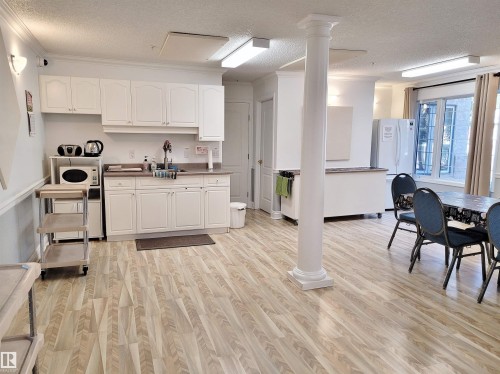 Kitchen featuring a textured ceiling, white cabinetry, crown molding, light wood-type flooring, and freestanding refrigerator - 404 13450 114 Avenue, Edmonton, AB - Indoor